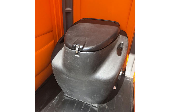 Geschlossene tragbare Toilette aus schwarzem Kunststoff in einem orangefarbenen Raum